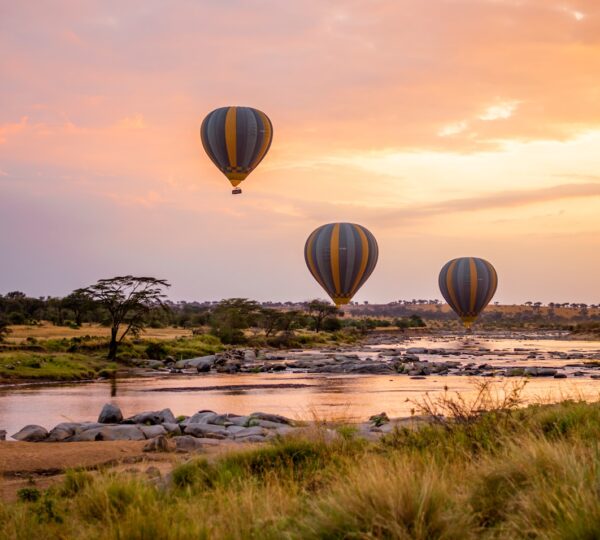 three hot air balloons flying over a river